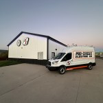 White and Orange Pro Circuit Electric Van in front of Pro Circuit building.